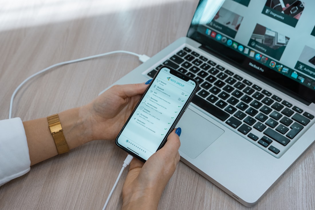 A woman is using her cell phone while sitting in front of a laptop